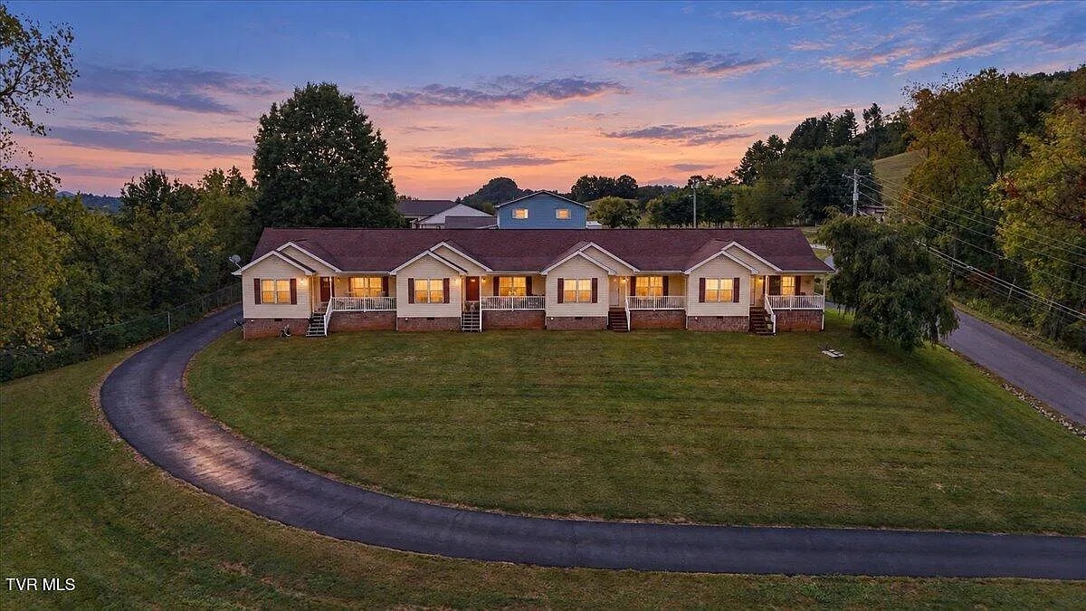 The quadplex apartment building under contract, glowing at sunset with a curved driveway and a green lawn